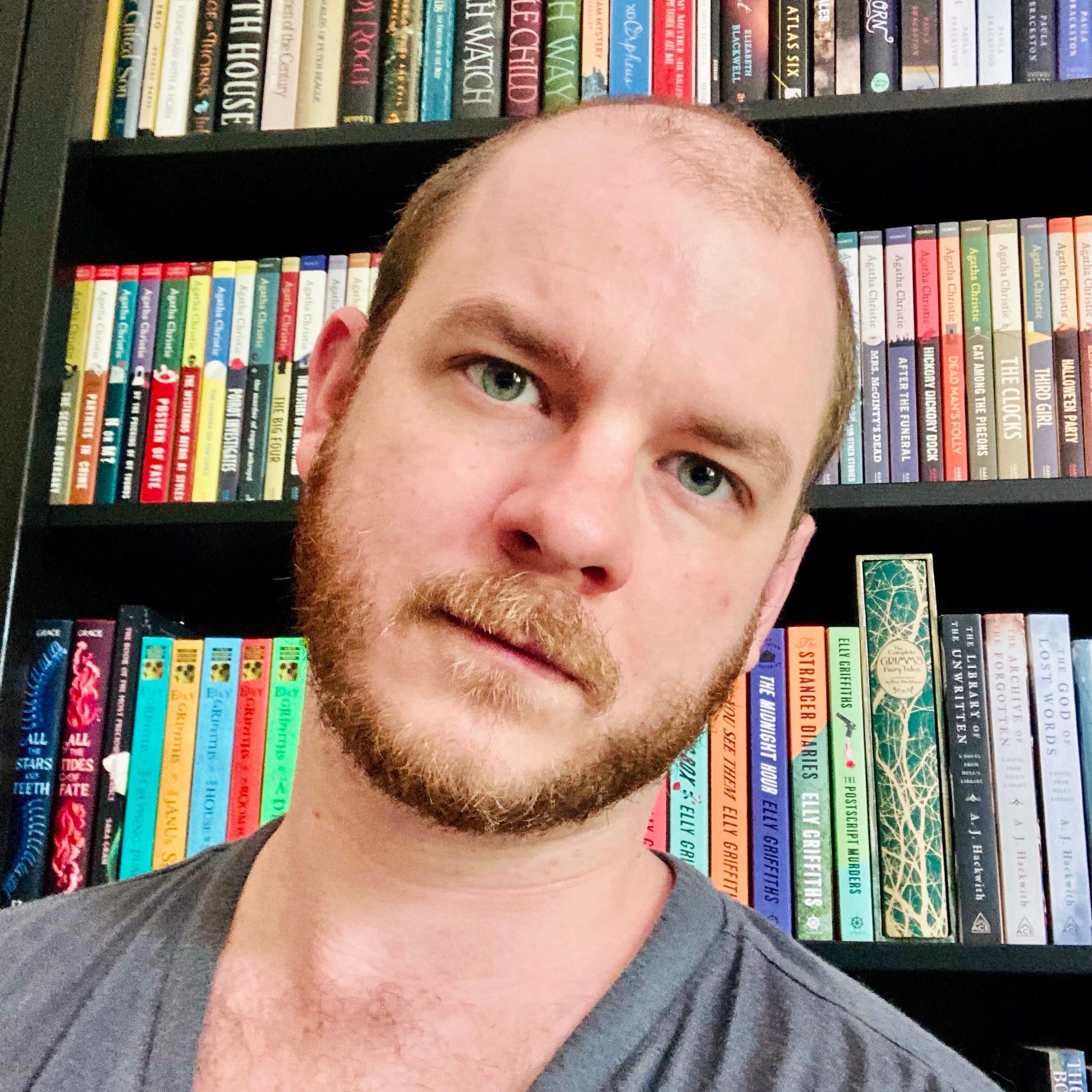 A man in a gray shirt with books in the background
