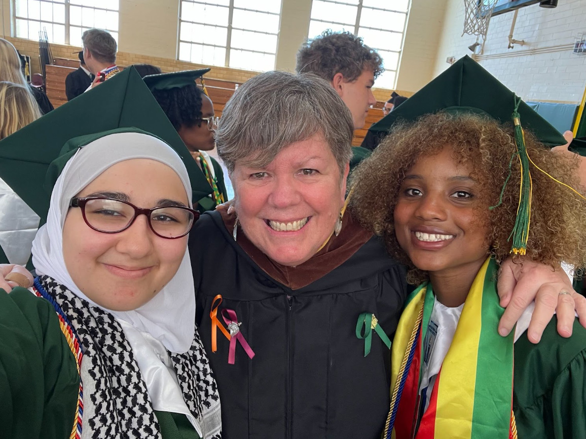 Patty Smith stands between two students wearing caps and gowns