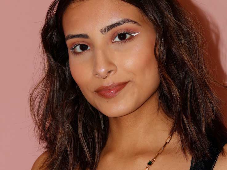 Fabiana Acosta smiles and stands against a blush pink wall.