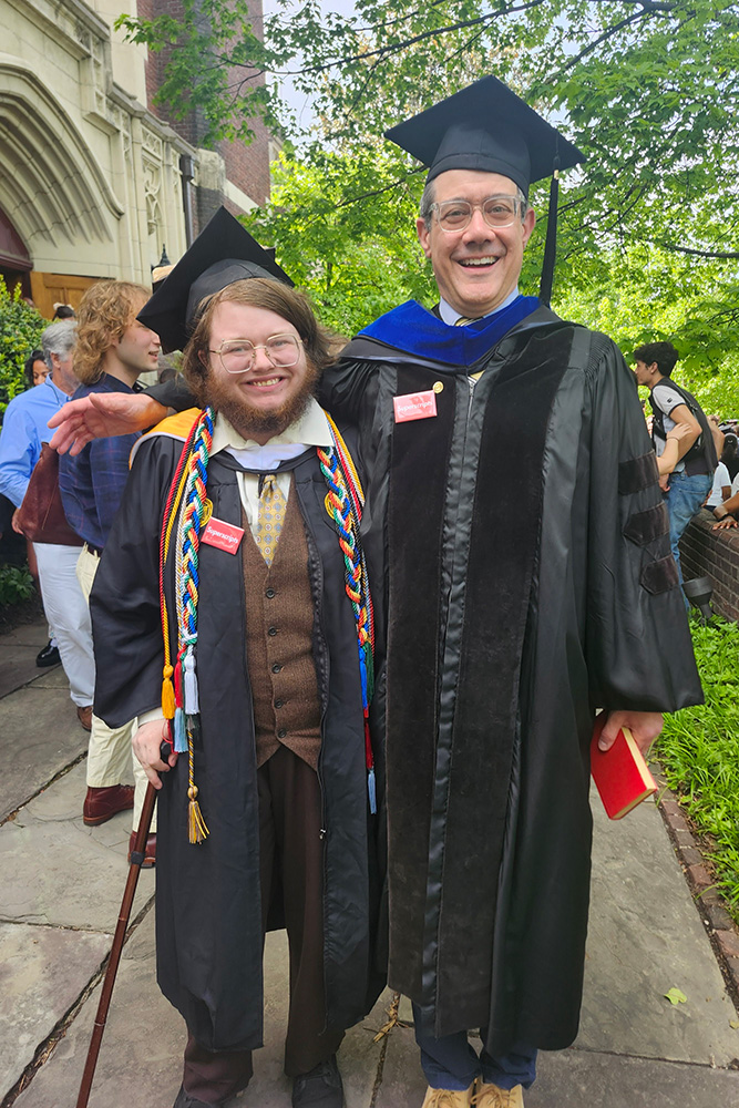 Cael Sinclair stands next to a professor, both wearing graduation regalia
